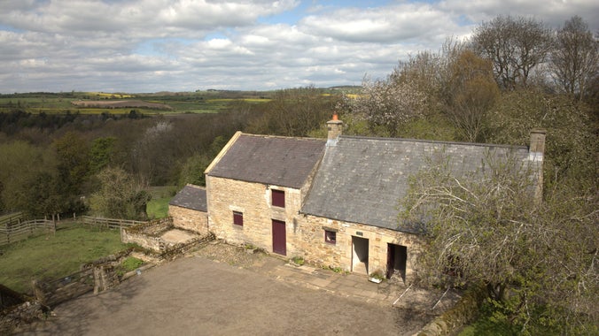 An 18th century stone built cottage with green fields and trees behind